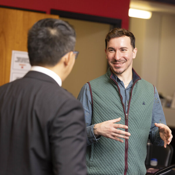 Two men smiling and talking in an indoor setting with informational materials on a table